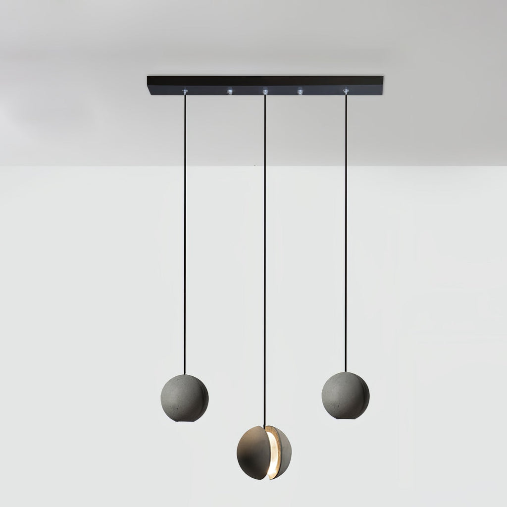 Three Clérachic concrete pendants hang from a long black bar canopy, the middle one lowest and lit through its slot.