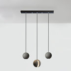 Three Clérachic concrete pendants hang from a long black bar canopy, the middle one lowest and lit through its slot.