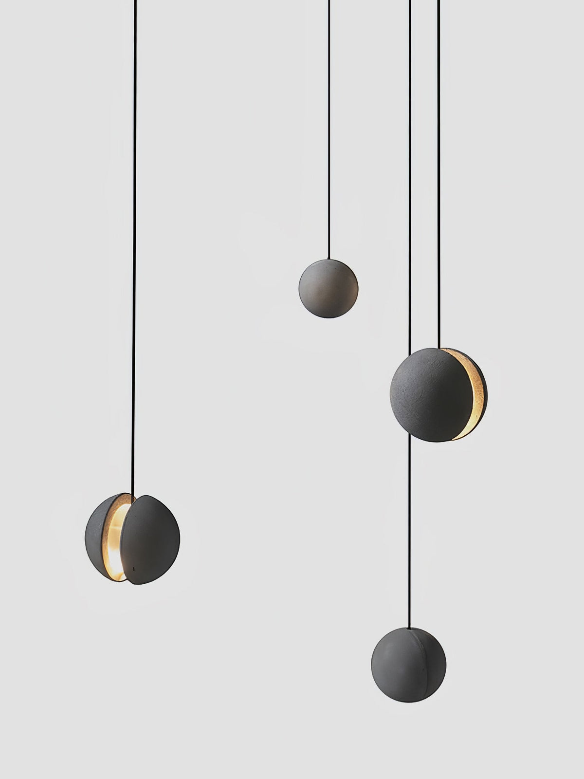 Four Clérachic concrete pendants hang at different heights against light grey, two of them with a warm lit slot.