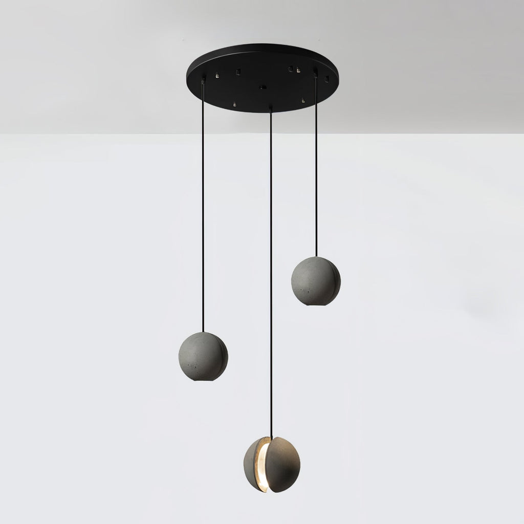 Three Clérachic concrete pendants hang from a round black canopy against a white wall, the lowest lit at its slot.