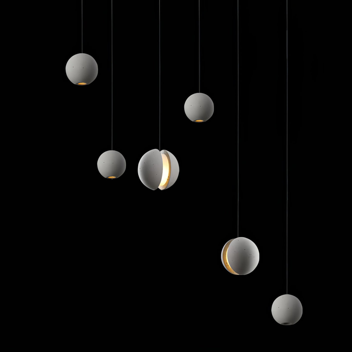 Six Clérachic concrete spheres hang against black, pale grey in tone, with two showing a bright lit crescent.