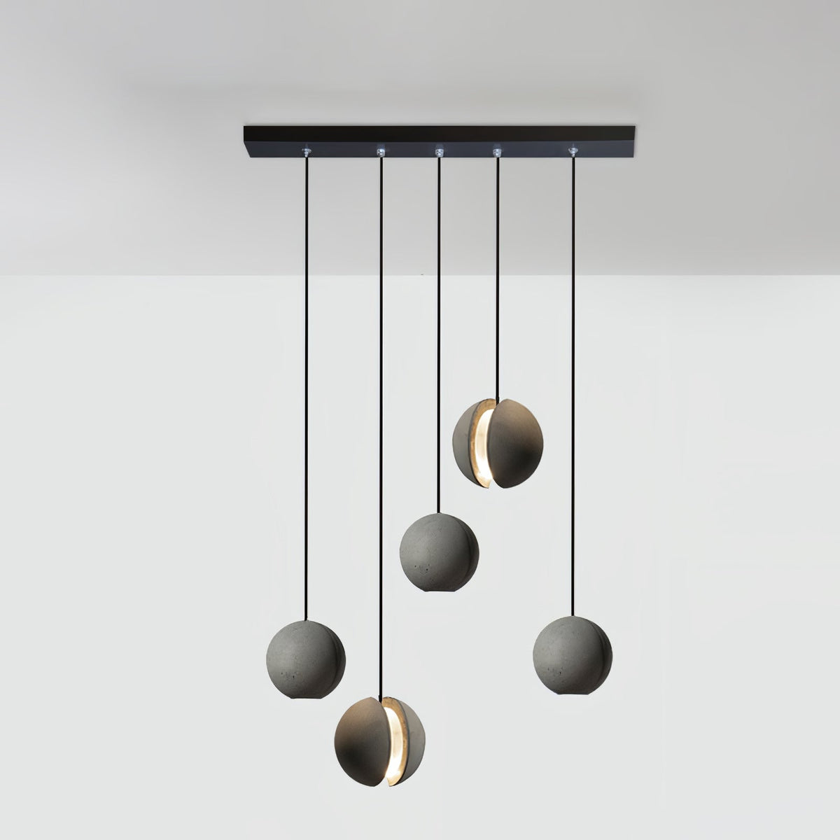 Five Clérachic concrete pendants hang from a long black bar canopy at staggered drops, two with a glowing slot.