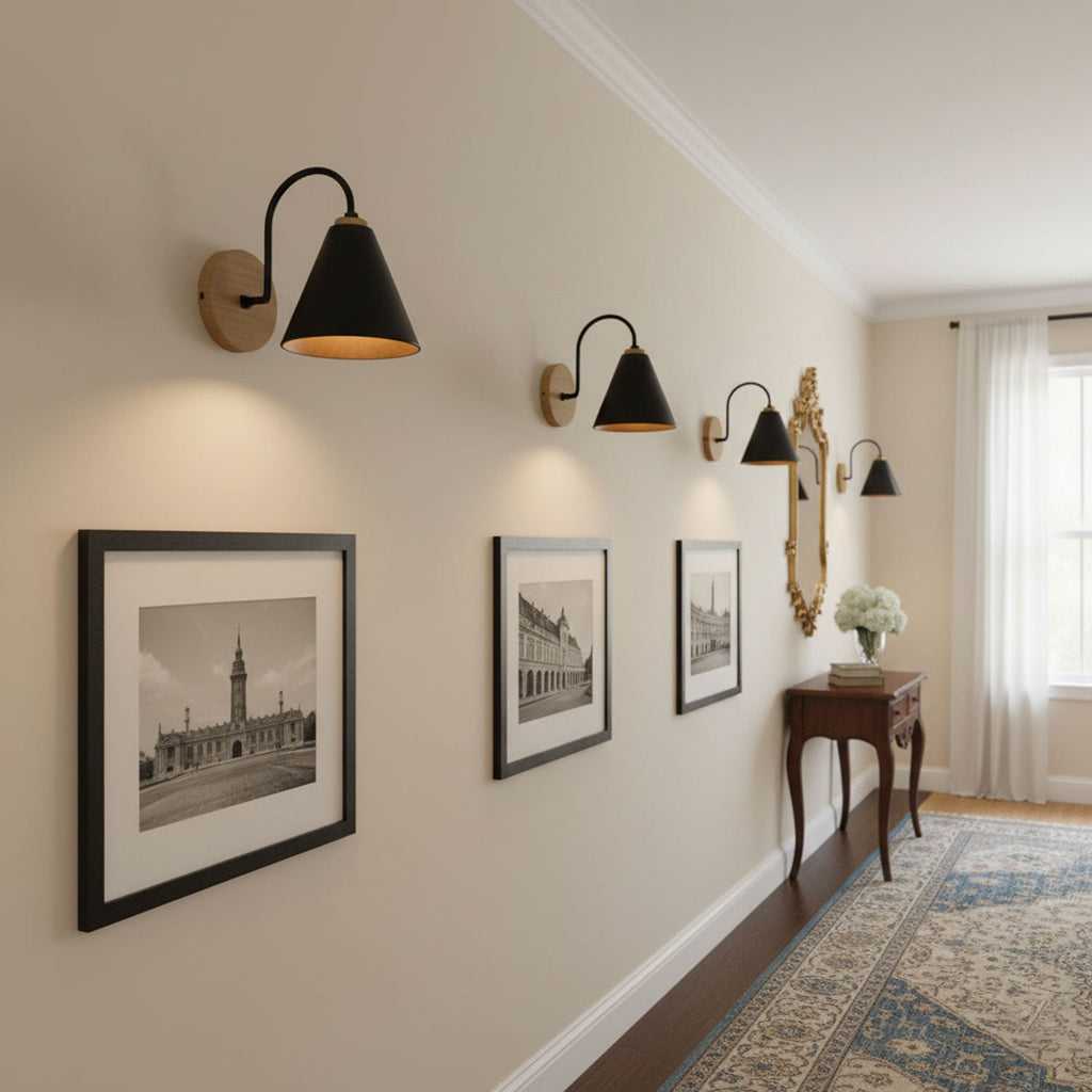 A row of black cone-shaded Clérachic wall lights along a cream hallway wall, beside framed black-and-white prints and a console table.