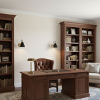 Two black Clérachic wall lights flank bookcases in a study, with a dark wood desk and a brass desk lamp below.