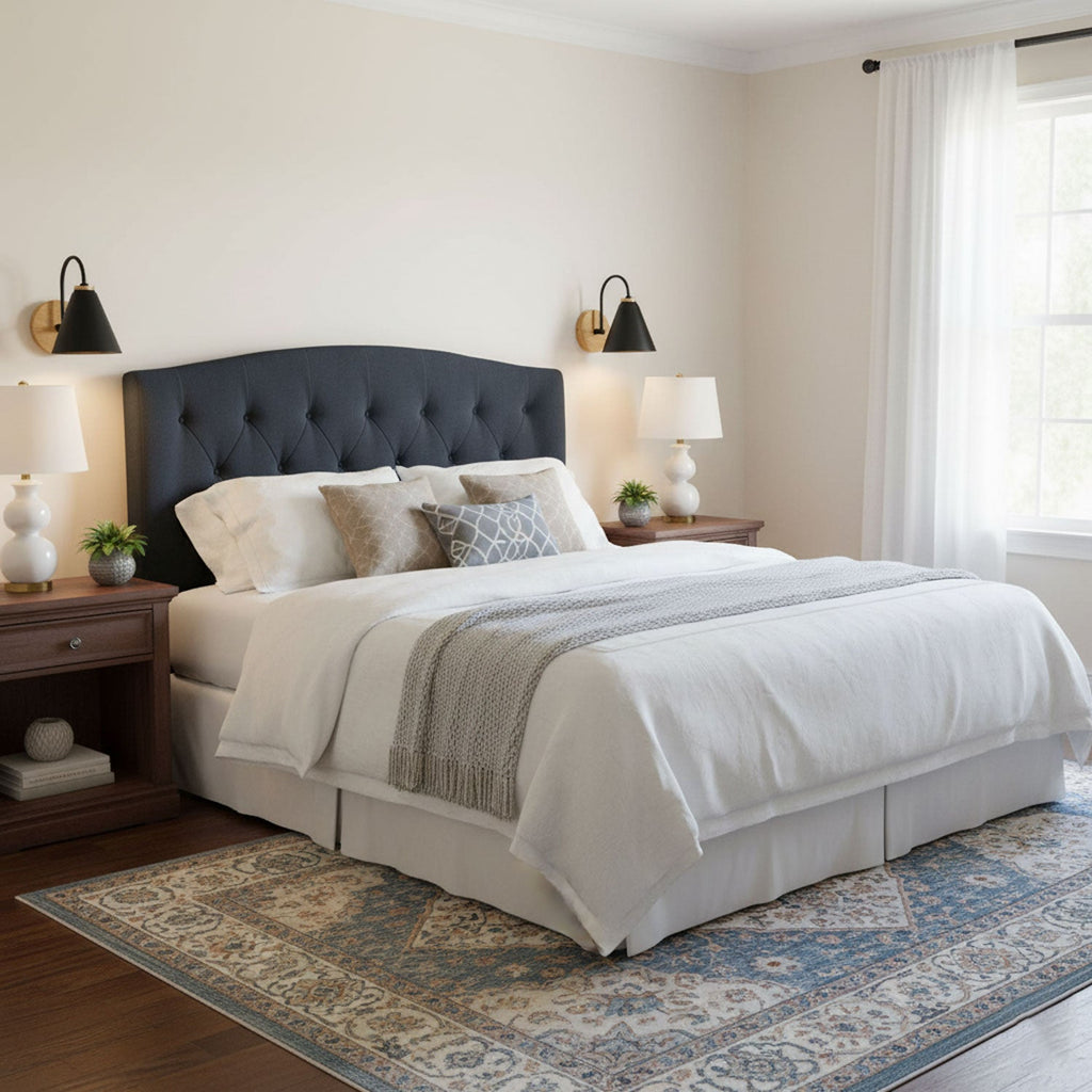 Black Clérachic wall lights on either side of a navy tufted headboard, with white bedside lamps and a pale bedspread.