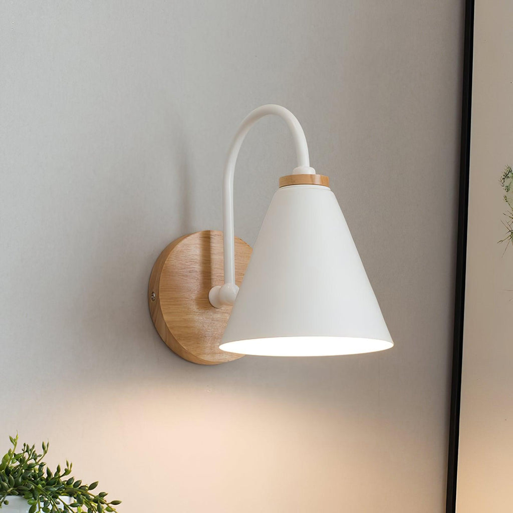 Close view of this white Clérachic wall light with a curved stem, glowing softly on a grey wall with a plant at lower left.