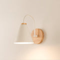 A cream-white Clérachic wall light with a round wooden backplate lit warmly against a peach-toned wall.