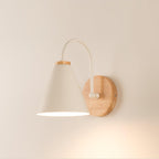 A cream-white Clérachic wall light with a round wooden backplate lit warmly against a peach-toned wall.