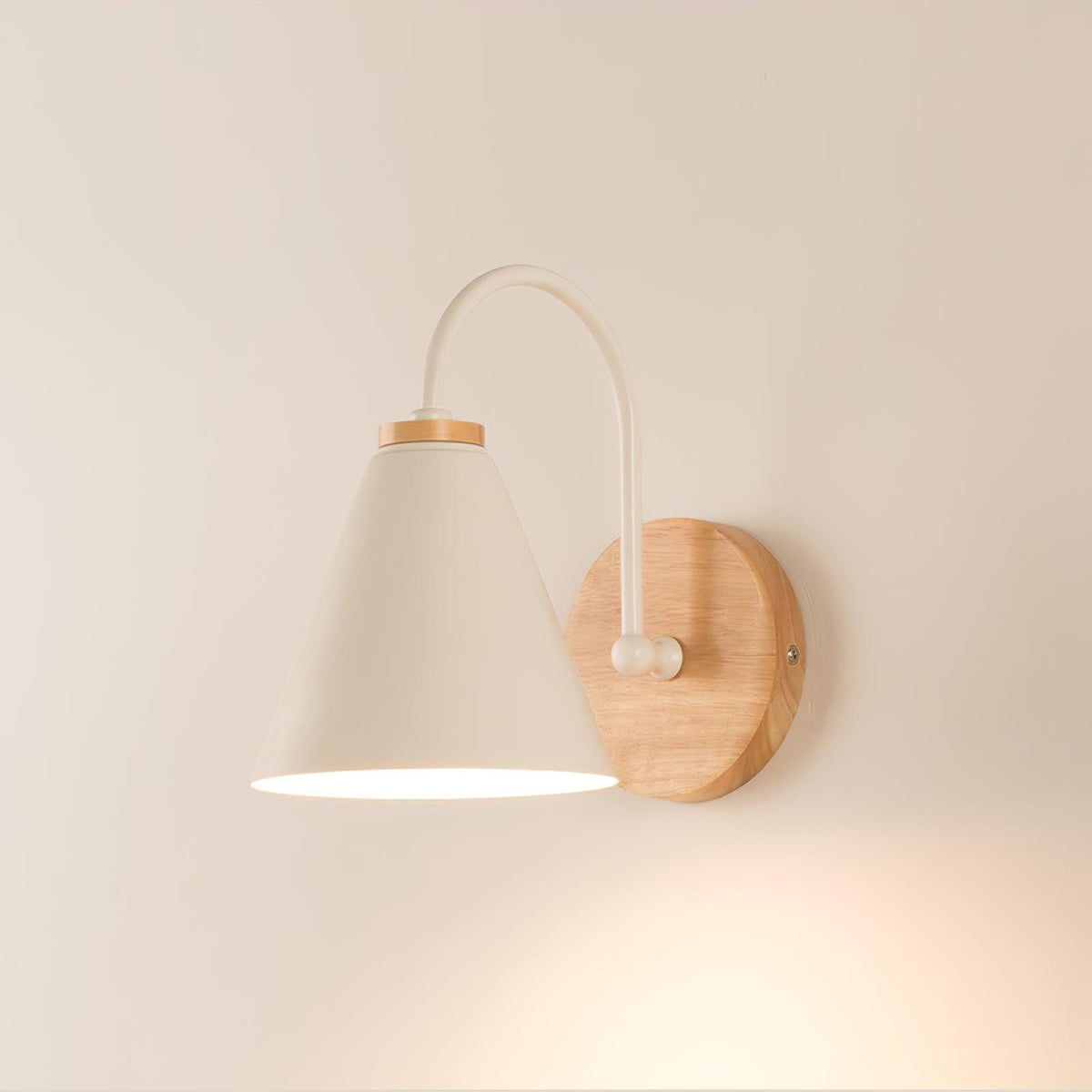 A cream-white Clérachic wall light with a round wooden backplate lit warmly against a peach-toned wall.