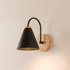 Black cone shade, curved stem and wooden backplate on a warm cream wall, this Clérachic wall light lit from inside.