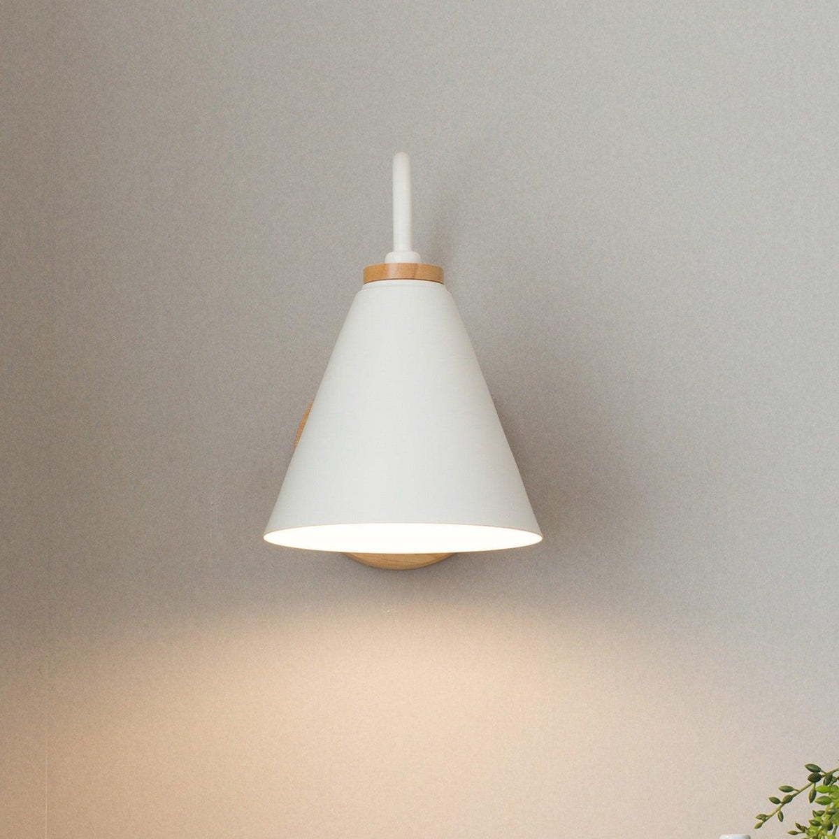 White cone shade with a short upturned stem, this Clérachic wall light seen from the front on a grey wall.