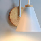 Wooden backplate with visible screws and the white cone shade of this Clérachic wall light, shown from the side with a warm glow.