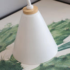 Close view of the white cone shade and wooden collar of this Clérachic wall light, over a cactus-print picture.