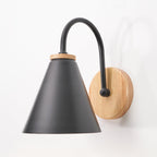 Close view of a black cone shade, wooden collar and wooden backplate on this Clérachic wall light, against a white wall.