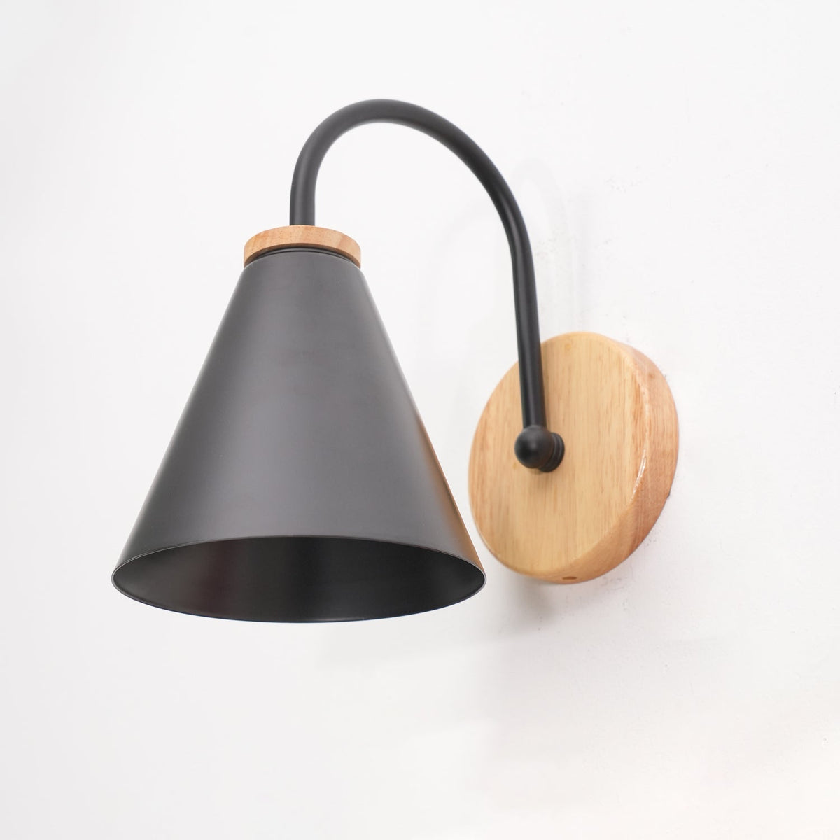 Inside view of the black cone on this Clérachic wall light, with the curved stem and wooden backplate behind it.