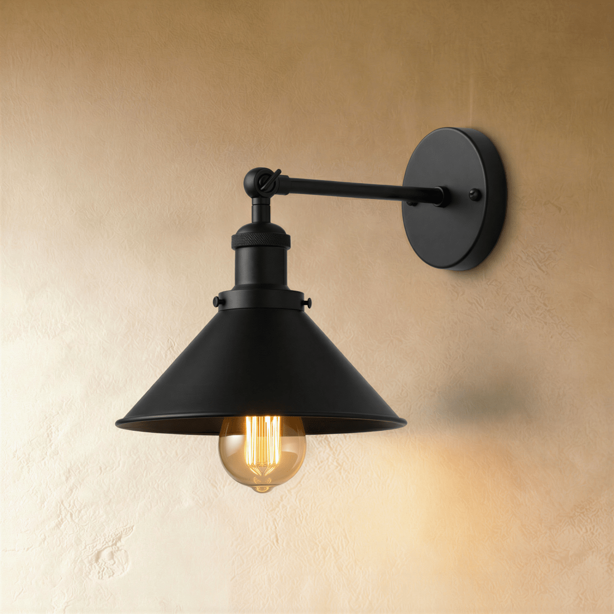 Clérachic all-black wall lamp with a wide cone shade, jointed arm and round backplate, lit by a warm filament bulb.