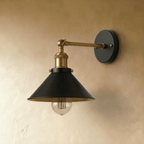 Clérachic wall lamp with a wide black cone shade, brass-toned arm and black backplate, shown with the filament bulb unlit.
