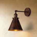 Clérachic wall lamp in a dark mottled rust-brown finish with a narrow cone shade and a gold-toned inside on a plaster wall.