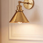 Close view of a Clérachic brushed brass wall lamp: wide cone shade, knurled collar and jointed arm against white moulding.