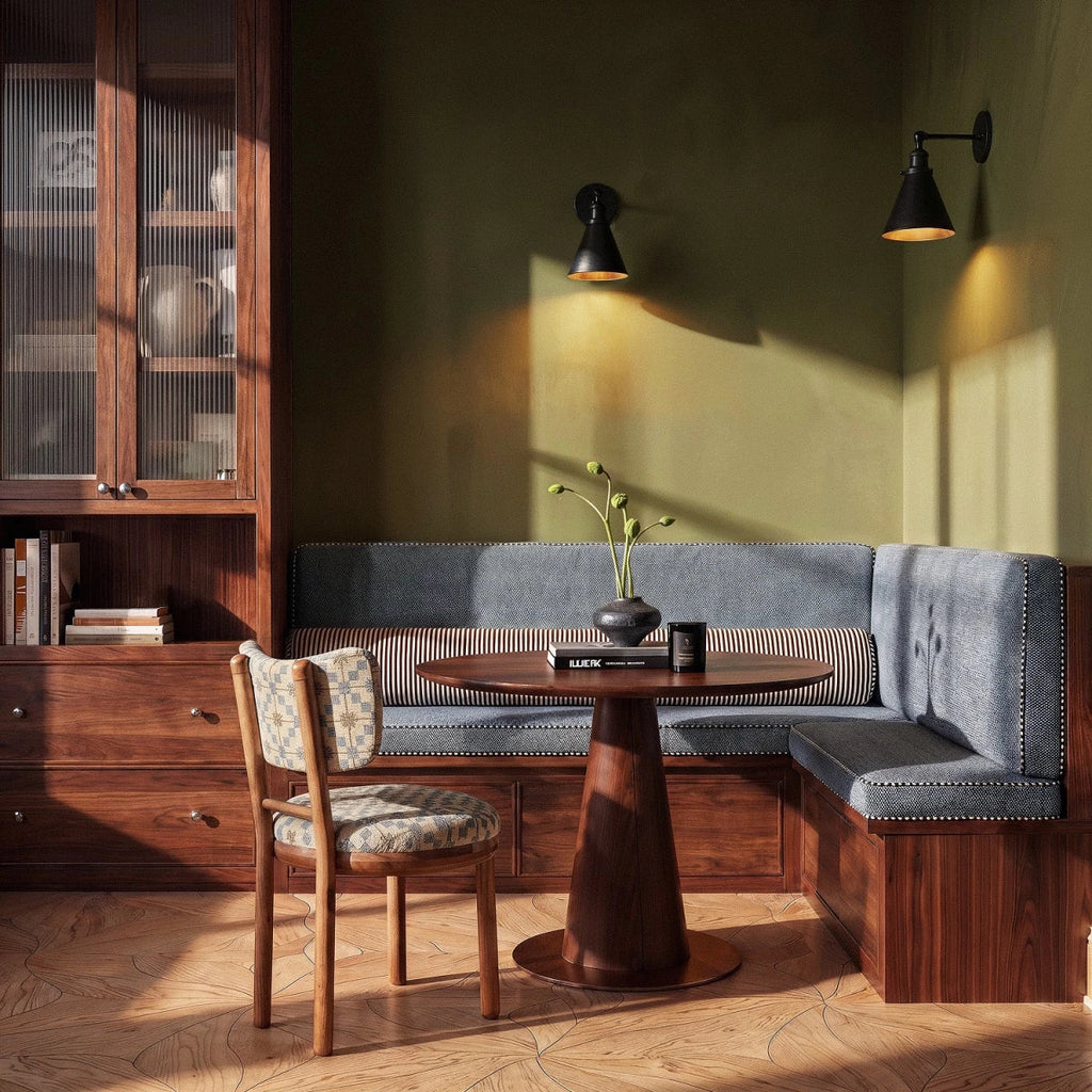 Two Clérachic black narrow-cone wall lamps with gold interiors washing an olive green wall above a walnut dining corner.