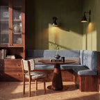 Two Clérachic black narrow-cone wall lamps with gold interiors washing an olive green wall above a walnut dining corner.