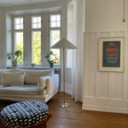 Clérachic floor lamp with a white cone shade in a bay-window corner, beside a cream sofa and a patterned round pouffe.