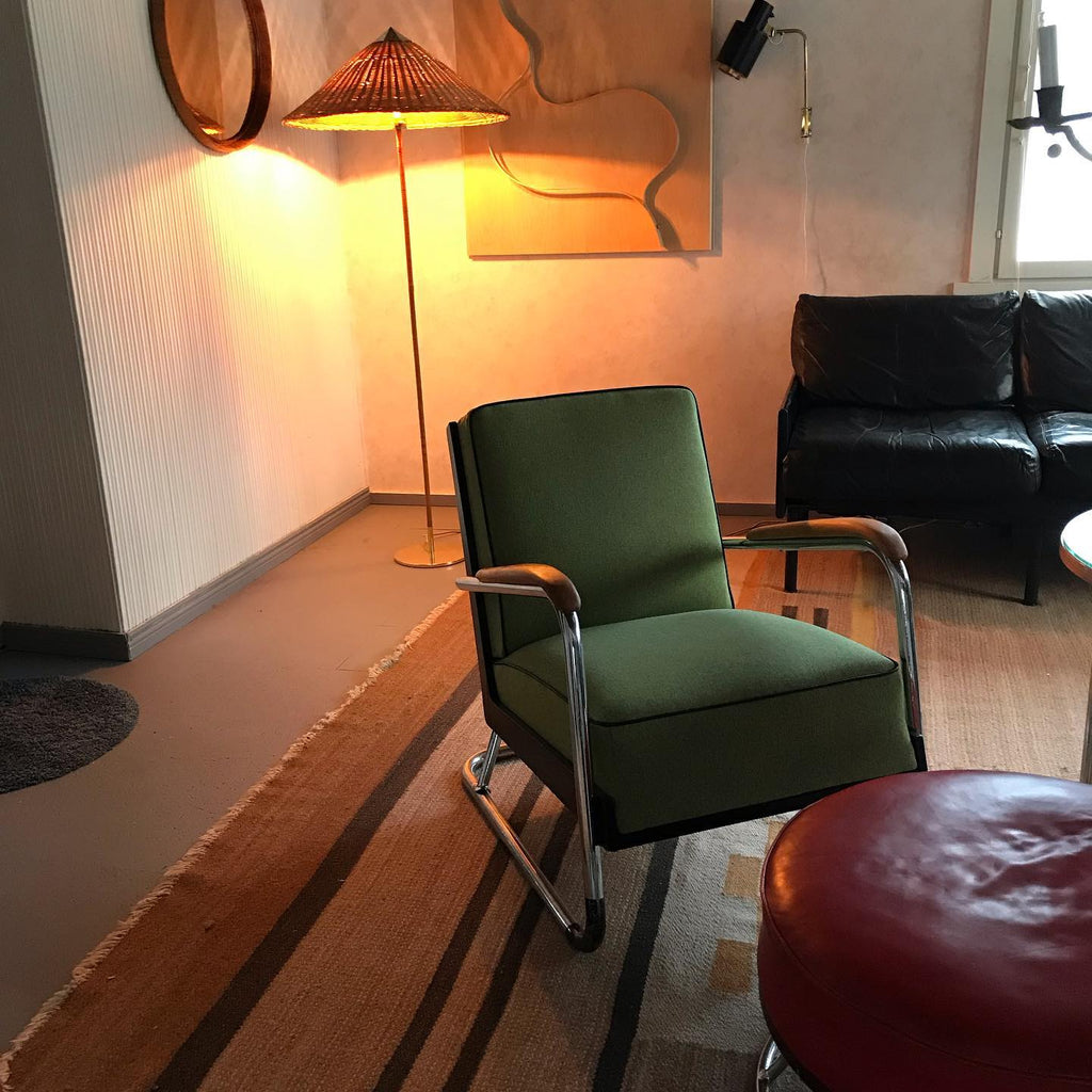 Clérachic floor lamp with a glowing rattan cone shade in a warm room with a green armchair and a black leather sofa.