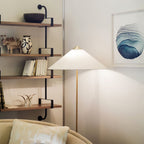 Clérachic floor lamp with a white cone shade beside a wall shelf of ceramics and books, with a blue abstract print behind.