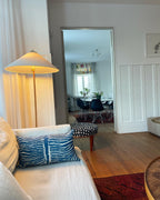 Clérachic floor lamp with a warm-lit cone shade in a hallway view, above a sofa cushion with a blue pattern and a red rug.