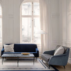 Clérachic floor lamp with a white cone shade in front of a tall arched window, between a navy sofa and a blue-grey sofa.