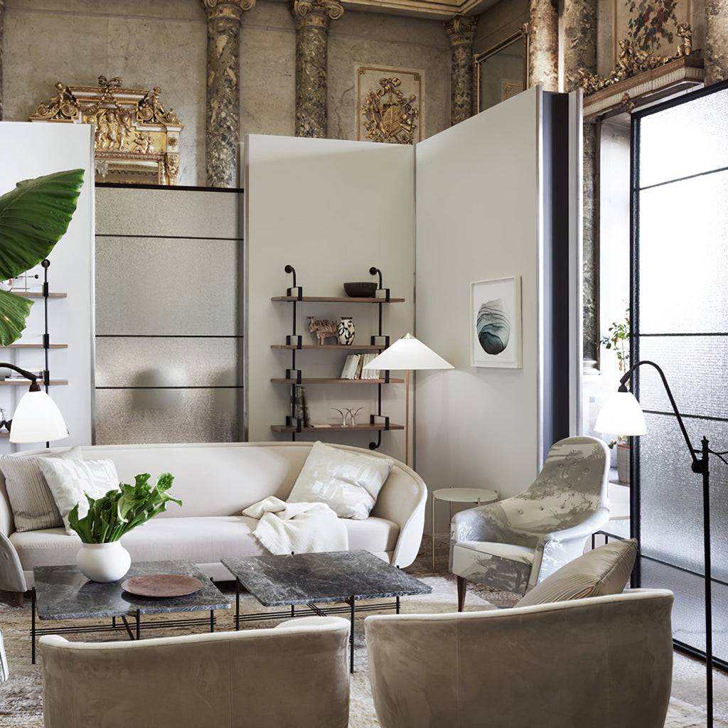 A Clérachic floor lamp among several lights in an ornate room, behind a cream sofa, a stone-top coffee table and armchairs.
