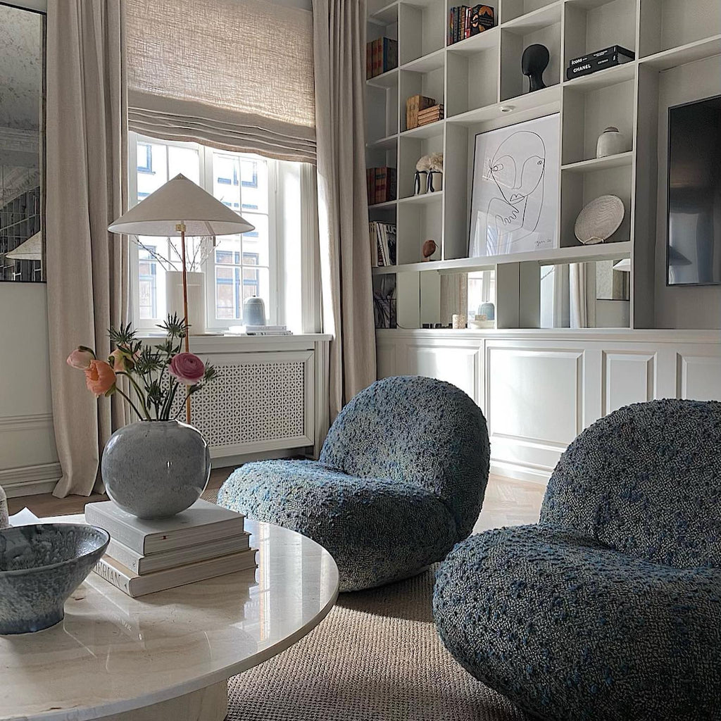 Standing floor lamp from Clérachic with a white cone shade by a window, above a round table with flowers and two speckled-blue chairs.