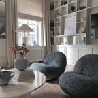 Standing floor lamp from Clérachic with a white cone shade by a window, above a round table with flowers and two speckled-blue chairs.