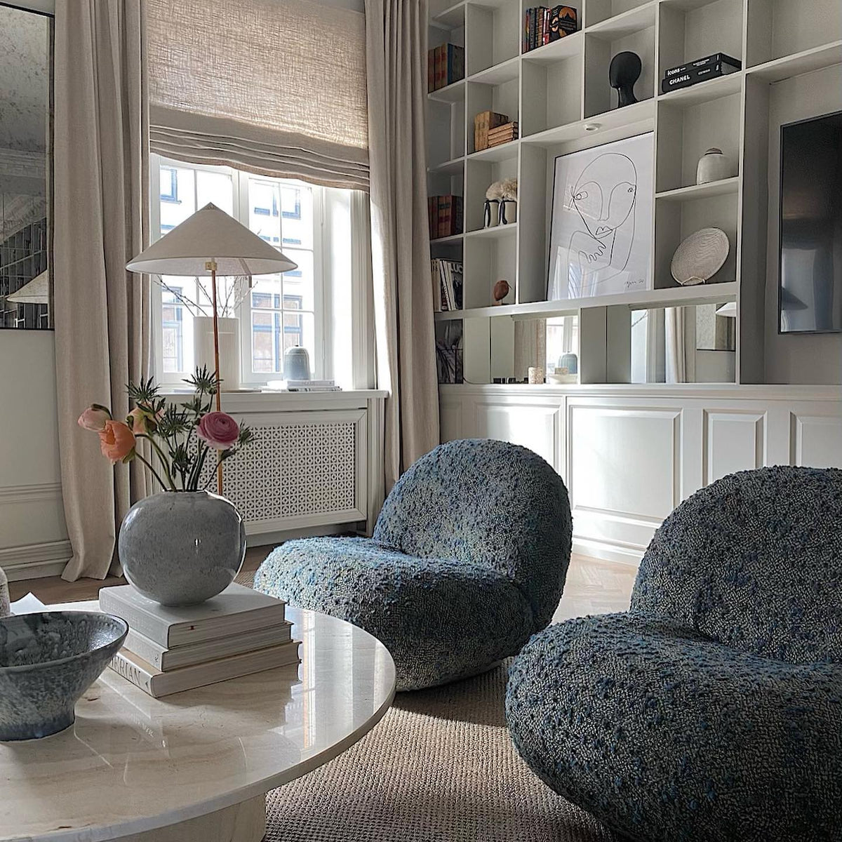 Standing floor lamp from Clérachic with a white cone shade by a window, above a round table with flowers and two speckled-blue chairs.