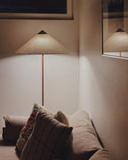 Close crop of a Clérachic floor lamp with a woven-textured cone shade, above a sofa with patterned cushions.