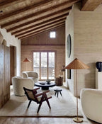 Clérachic floor lamp showing a woven rattan cone shade in a beamed attic room, beside bouclé chairs and a low black table.