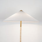Close view of the Clérachic floor lamp's white cone shade, brass collar and light rattan-wrapped stem, on a pale backdrop.