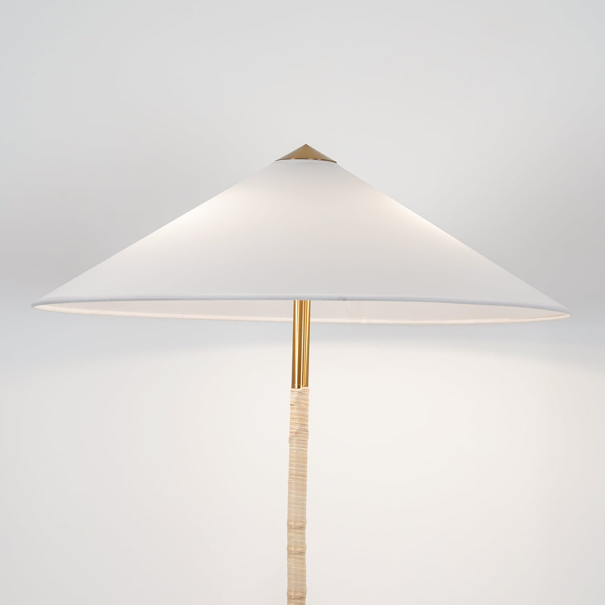 Close view of the Clérachic floor lamp's white cone shade, brass collar and light rattan-wrapped stem, on a pale backdrop.
