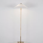 Clérachic floor lamp with a white cone shade, a light cane-wrapped stem and a brass base, on a pale grey backdrop.