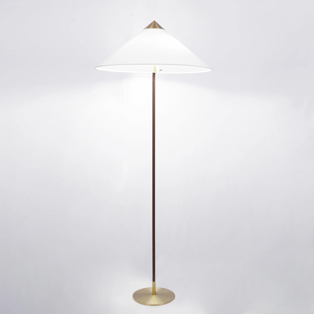 Clérachic floor lamp with a lit white cone shade, a dark brown wrapped stem and a brushed brass base, on a pale backdrop.