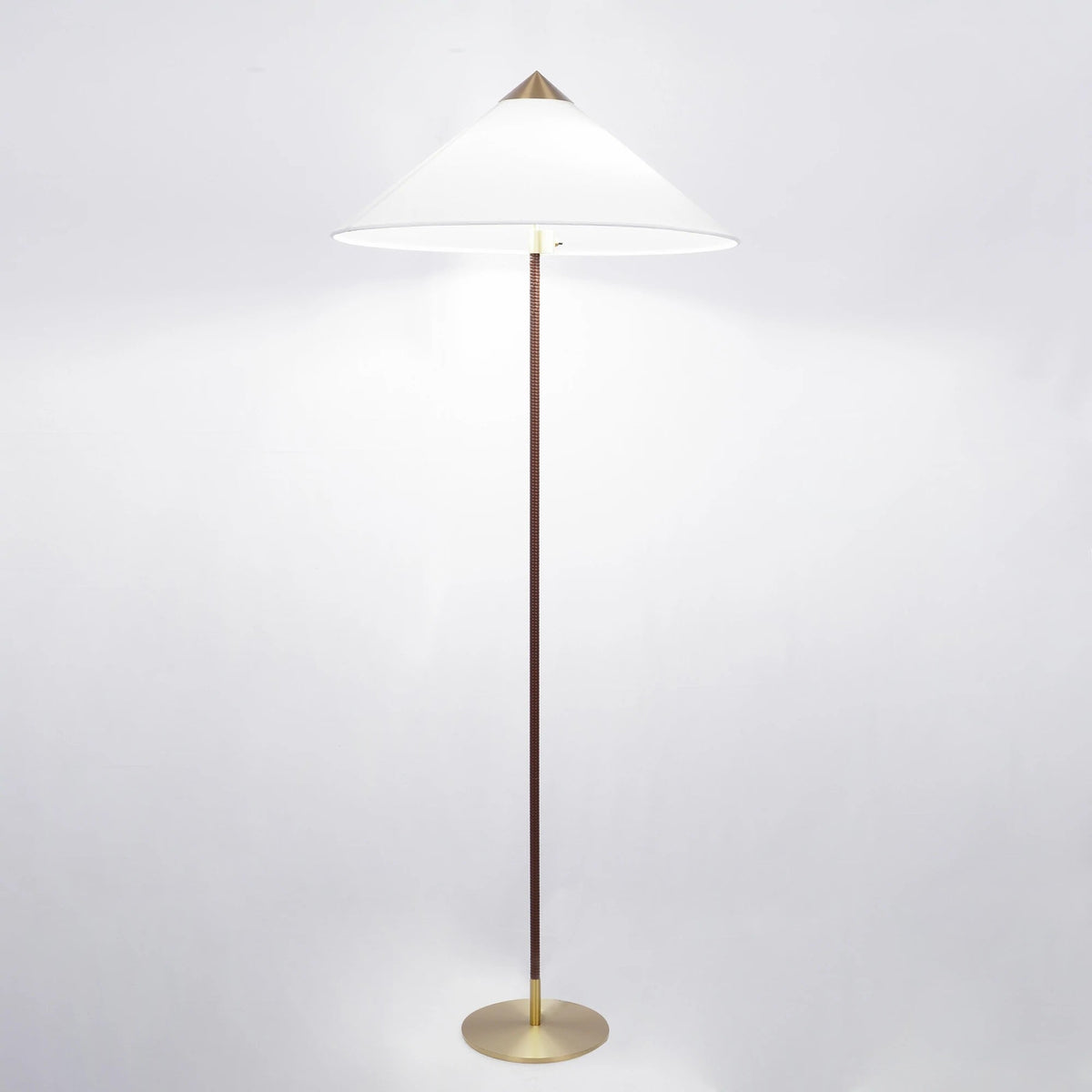 Clérachic floor lamp with a lit white cone shade, a dark brown wrapped stem and a brushed brass base, on a pale backdrop.