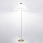 The Clérachic floor lamp with a white cone shade lit, its brown stem and brass base shown against a light grey backdrop.