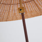 Close view of the brass switch plate where the brown leather-wrapped stem meets the woven rattan shade of this Clérachic lamp.