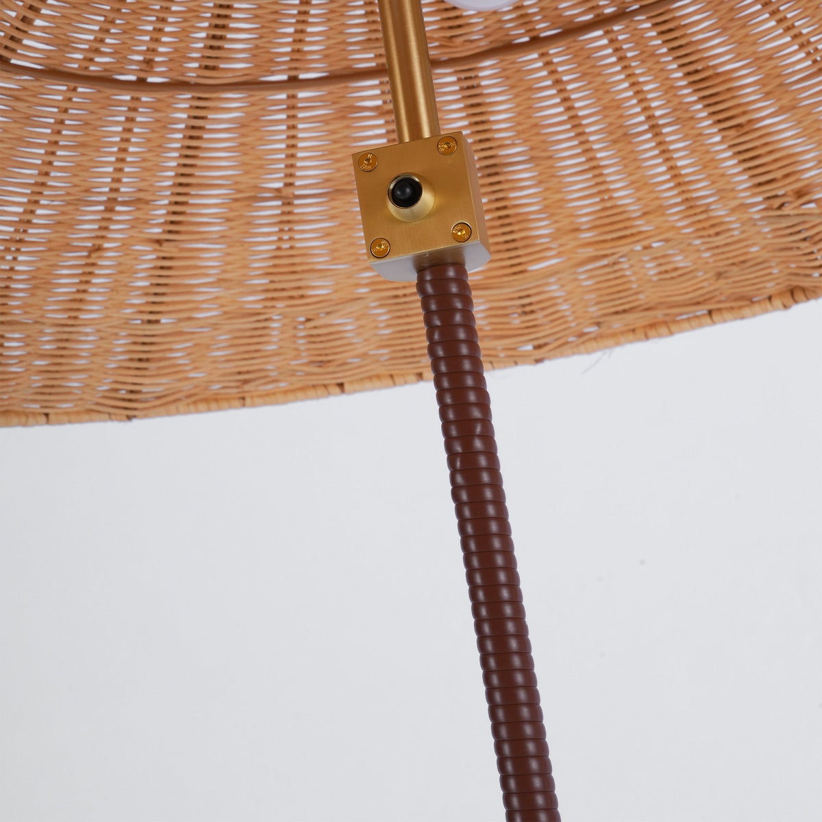 Close view of the brass switch plate where the brown leather-wrapped stem meets the woven rattan shade of this Clérachic lamp.
