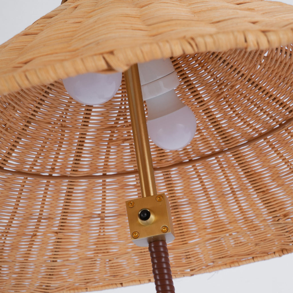 Looking up inside the rattan shade of this Clérachic floor lamp, where two bulbs sit above the brass switch plate.