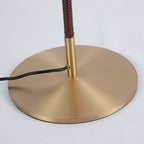 Close view of the round brushed brass base, the brown wrapped stem and the black cord on this Clérachic floor lamp.