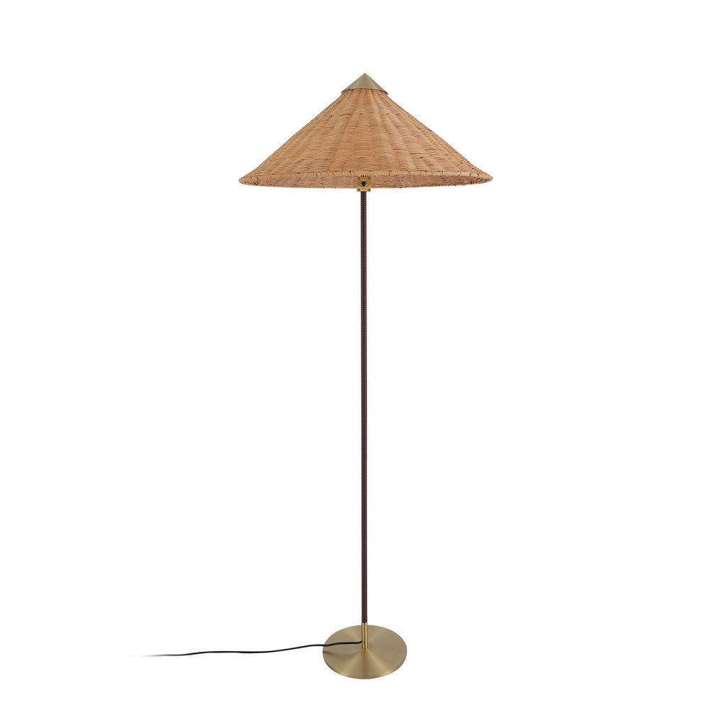 Clérachic floor lamp with a woven rattan cone shade and a thin dark stem, on a round brass base, on white.