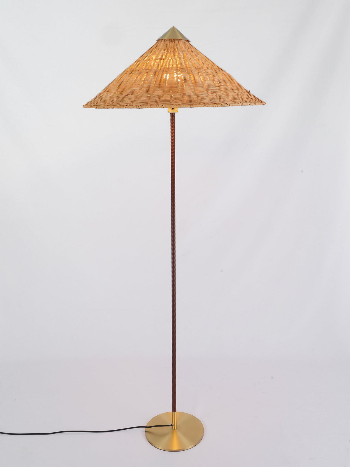 Standing floor lamp from Clérachic with a lit rattan cone shade, its black cord trailing across a pale grey floor.