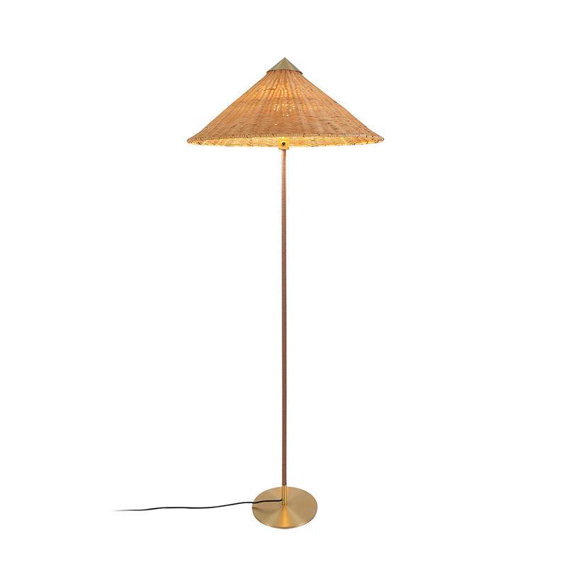 Tall Clérachic floor lamp with a rattan cone shade glowing at its rim, with a dark stem and a black cord, on white.