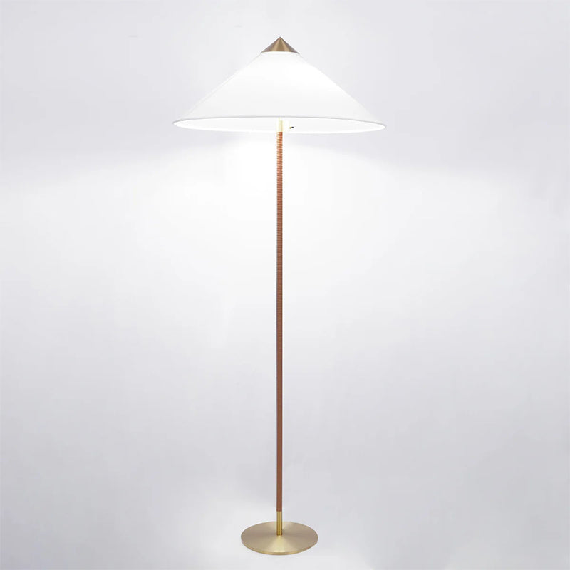 Clérachic floor lamp with a bright white cone shade casting light on a pale backdrop, its stem dark brown over a brass base.